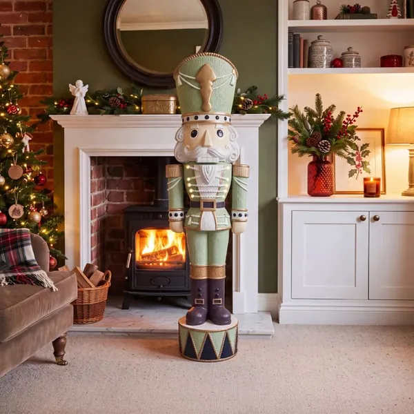 Whimsical Verde Otto nutcracker in sage green standing in front of a fireplace