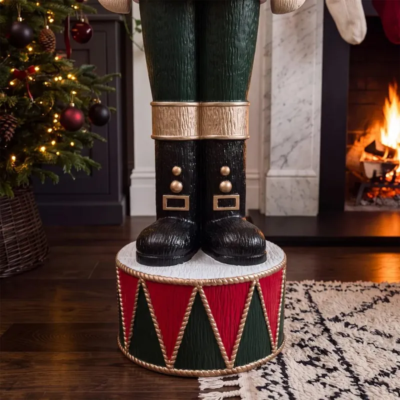Otto's black boots standing on his red and green drum base beside a Christmas tree and fireplace